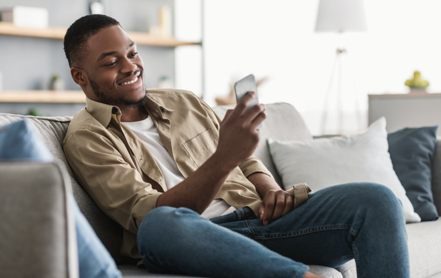 man sitting on couch looking at phone and smiling