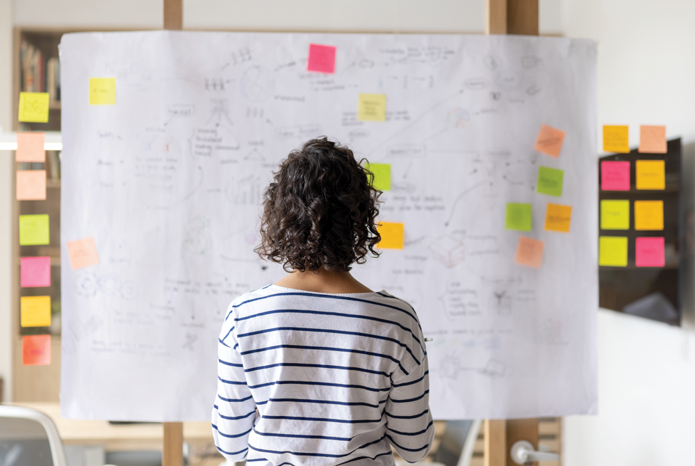 A person facing board with project management information and sticky notes.