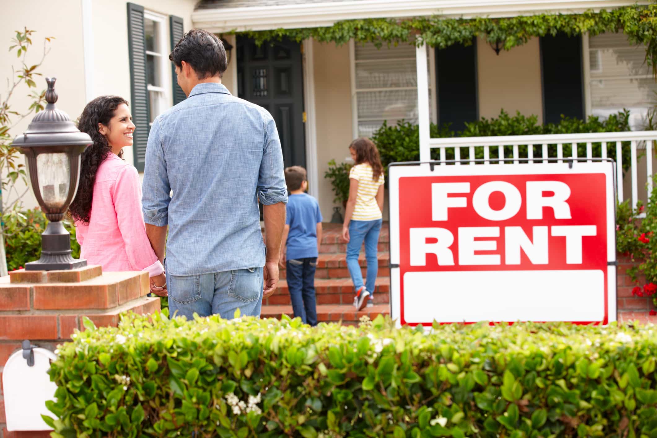 family outside house with "for rent" sign