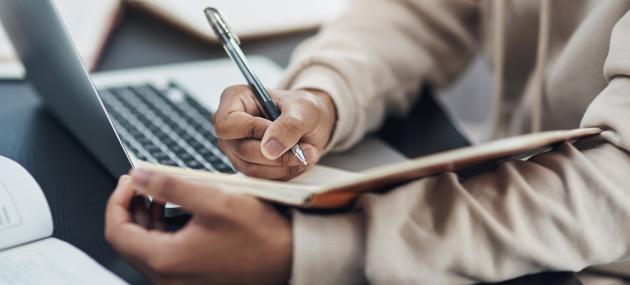 person taking notes in notebook while sitting at laptop