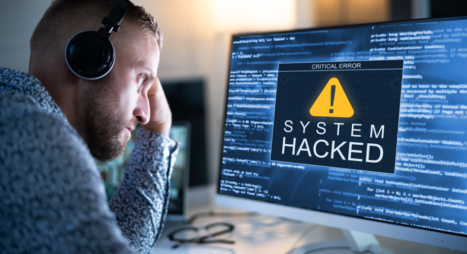 man in front of computer with big warning on the screen saying "System Hacked"