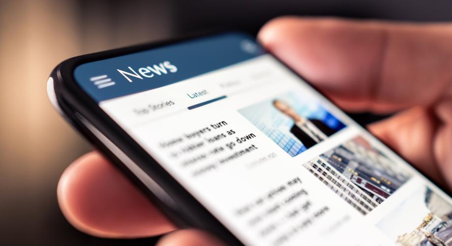 Photo of a person holding a cellphone, viewing a news app.