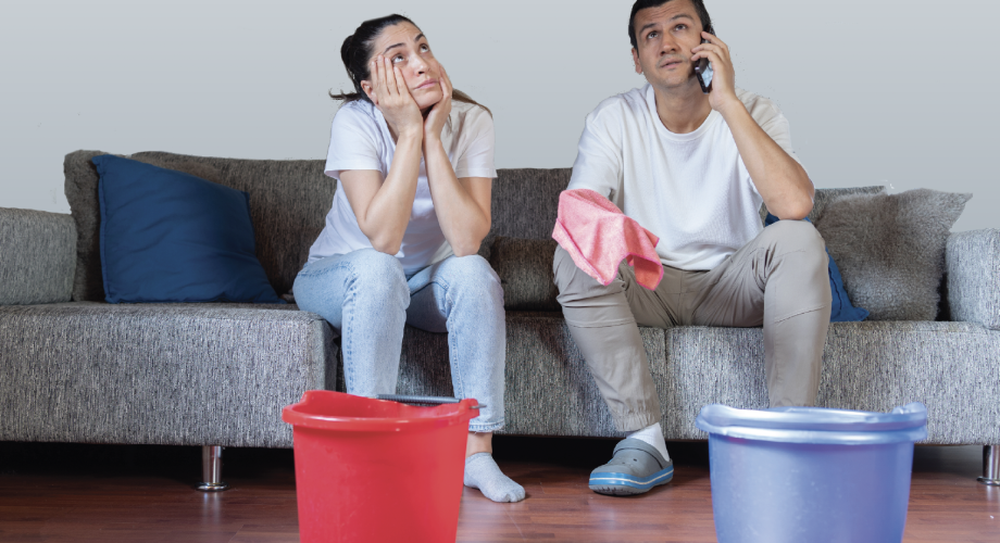 two people sitting on a couch looking up at the ceiling with buckets on the floor