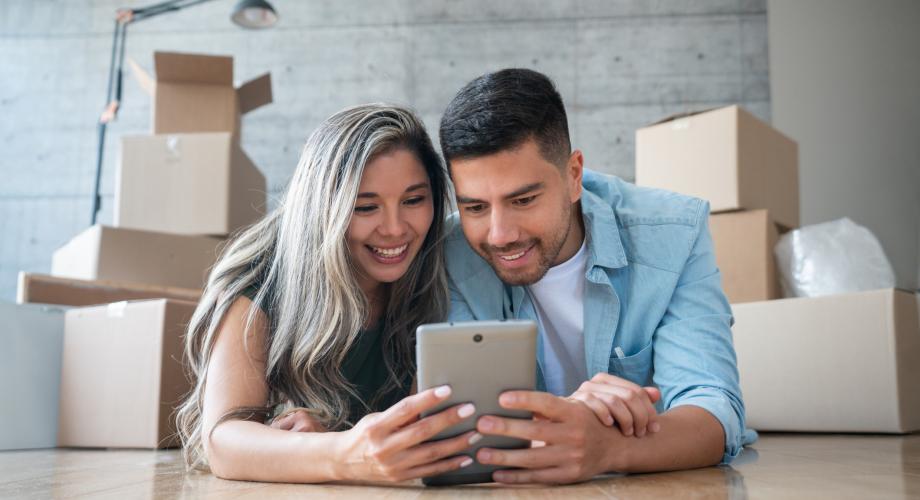 couple with moving boxes behind them looking at a tablet