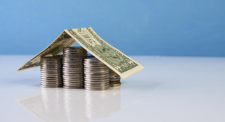 dollar bill and coins stacked in the shape of a house