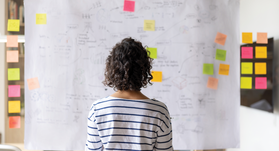 A person facing board with project management information and sticky notes.