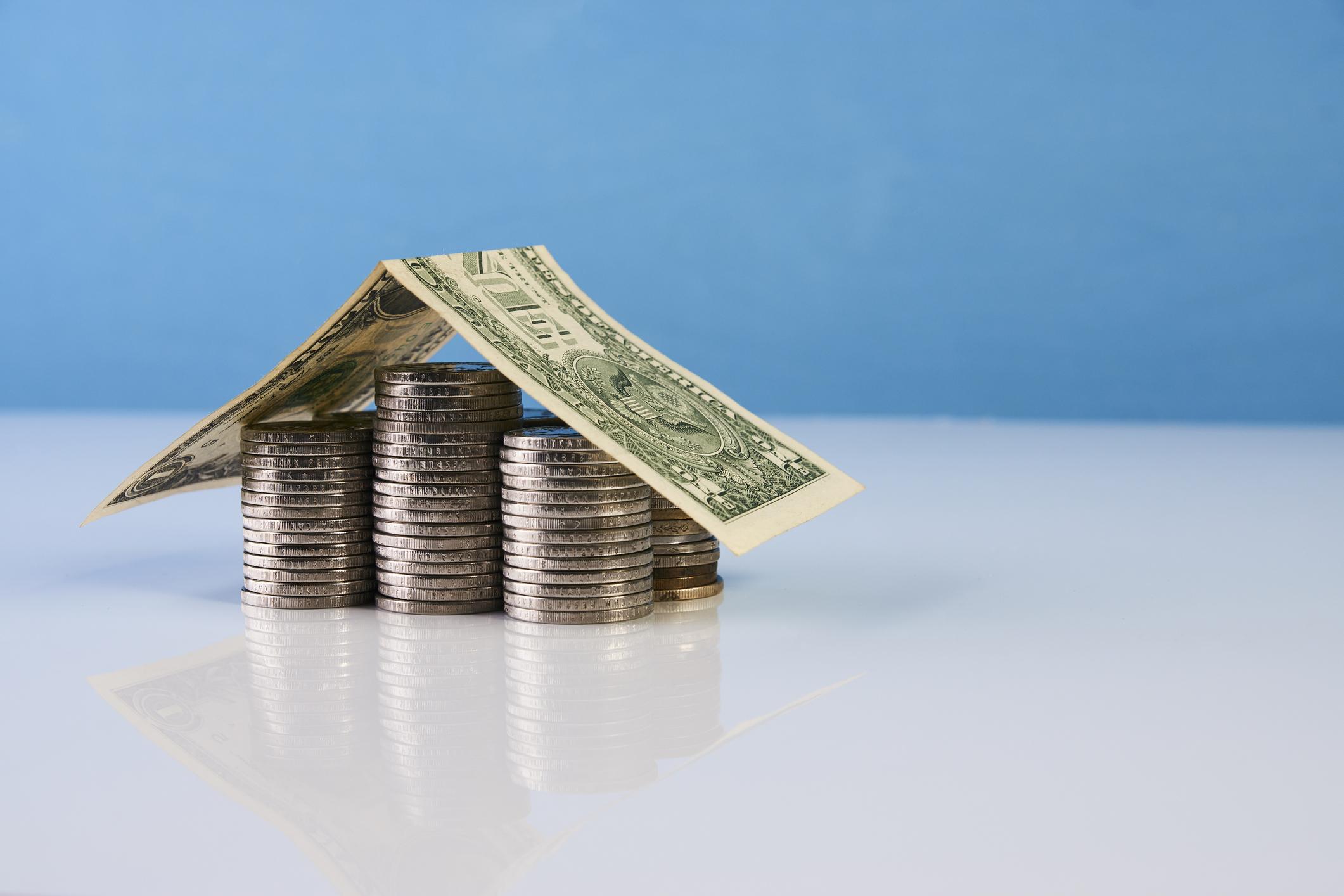 stack of coins with a folded dollar bill on top, resembling the shape of a house
