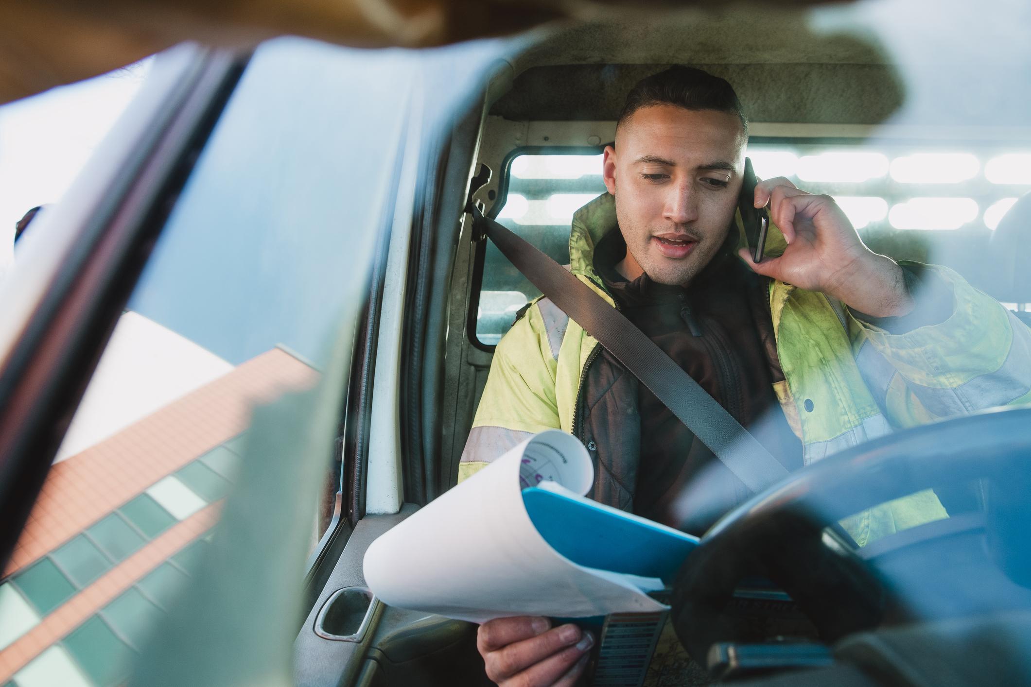 contractor in van looking at papers and talking on phone