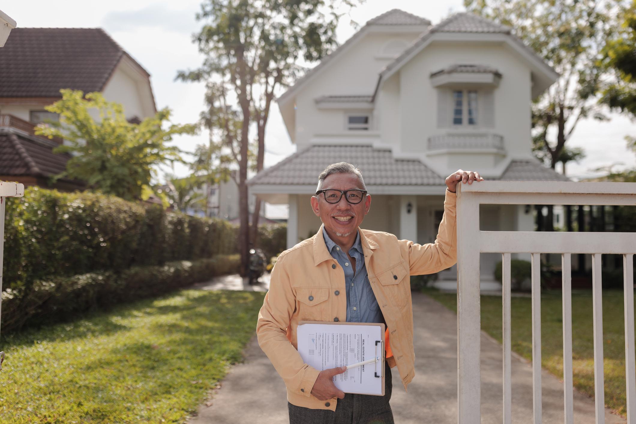 man standing in front of home with binder in his hand